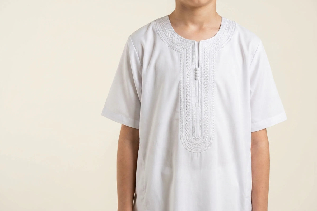 Qamis enfant blanc porté, encolure ronde bordée d'une broderie tressée