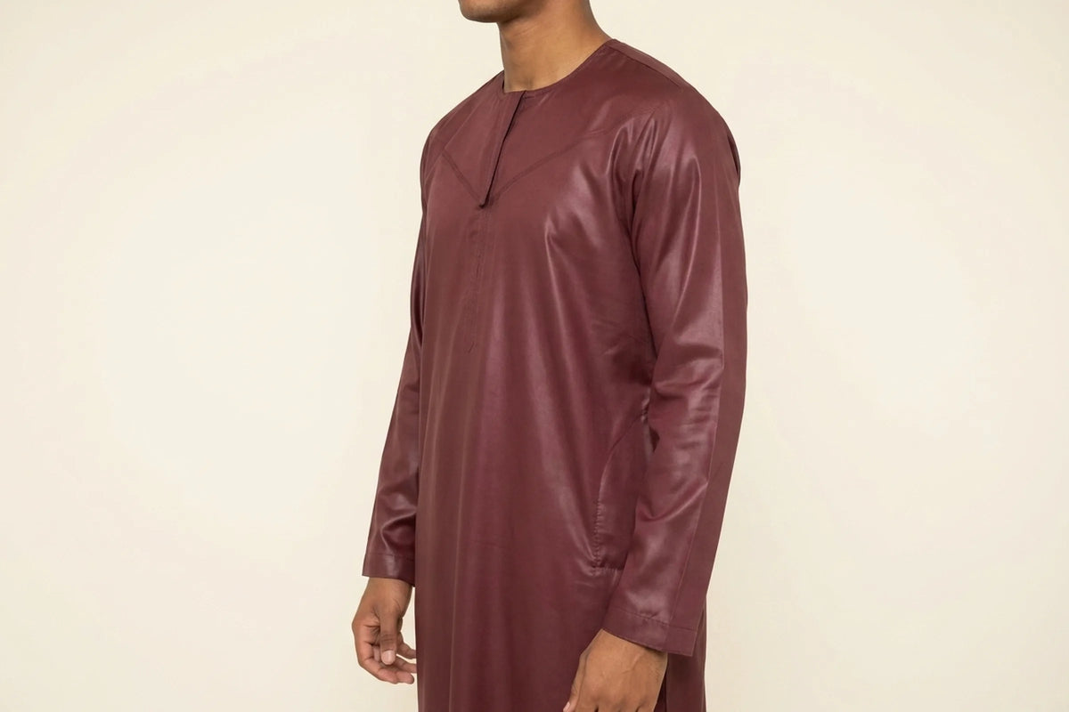 Qamis omani bordeaux porté, encolure sans col et satin qui accroche la lumière sur les plis