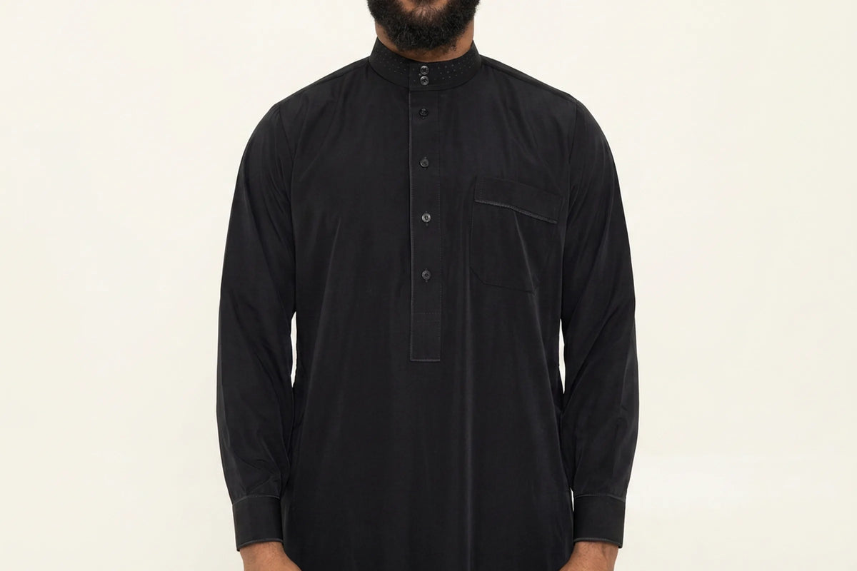 Qamis saoudien noir porté, col mao, patte boutonnée et poche poitrine passepoilée