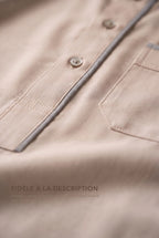 Macro du liséré gris et des boutons du qamis Issa beige, fidèle à la description