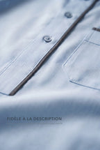 Macro du liséré et des boutons du qamis Issa bleu pastel, fidèle à la description