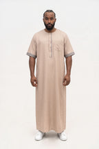 Qamis moderne beige Issa porté de face, manches courtes à revers et liséré gris sur la patte et la poche