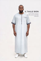 Qamis Issa bleu pastel en pied, coupe droite longueur cheville, il taille bien