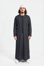 Qamis omani noir Hamza porté de face, encolure ronde sans col et tarboucha tressée ton sur ton